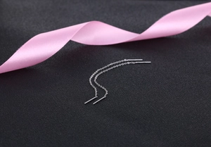 Close-up of S925 sterling silver tassel earrings on black texture with pink silk ribbon