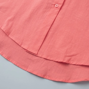 Detailed close-up of coral cotton linen shirt hem with matching button and fabric texture