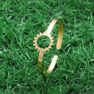 Detail of gold hollow open bangle featuring a sunburst design on polished stainless steel