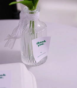 Close-up of vertical striped glass vase with lace ribbon and Thank You card tag