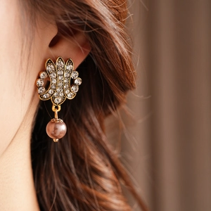 Close-up of vintage bronze earring with intricate hollow patterns and pink pearl pendant
