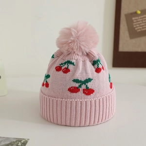 Close-up of pink knit hat featuring red cherry jacquard and fluffy faux fur pom-pom