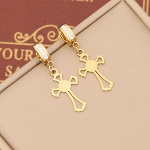Macro detail of gold-plated cross earrings with white zircon stones on beige box