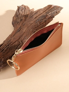 Minimalist brown leather card holder wallet with a metal zipper and keychain on wood