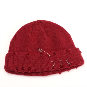 Detail of dark red knit beanie featuring silver metal rings, safety pin, and distressed holes