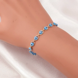 Detail of gold evil eye bracelet with blue charms worn on wrist against white silk