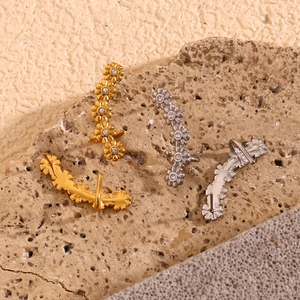 Detail of gold and silver floral ear crawlers with zircon centers on a stone surface