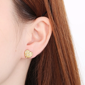 Close-up of golden heart-shaped stud earring with micro-set diamonds on ear