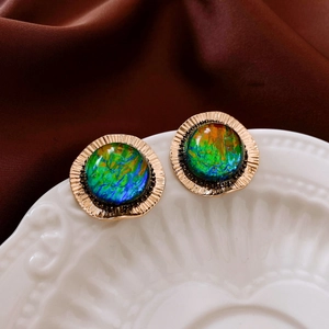 Close-up of vintage golden round stud earrings with iridescent rainbow gems on ceramic