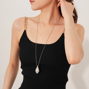 Detail view of a long silver bead chain necklace with a textured teardrop pendant on a model