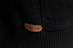 Detail of black knit fabric texture and premium brown leather label on the hemline