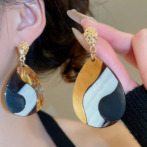 Close-up of model wearing large waterdrop earrings with gold metal and marbled resin detail