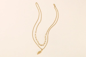 Detail of a double-layered gold necklace with a paperclip chain and leaf pendant