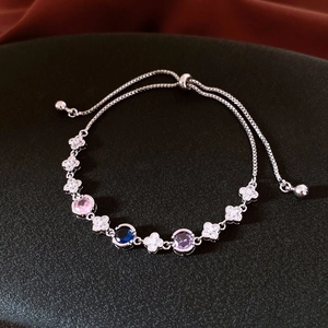 Detail of adjustable silver bracelet with colorful zircons and flower charms on black surface