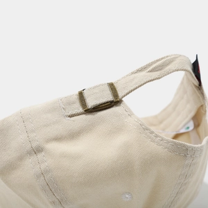 Detailed shot of beige cotton baseball cap featuring adjustable strap with bronze metal buckle