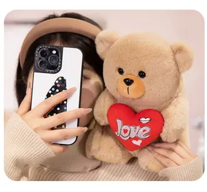 Close-up of a brown plush teddy bear holding a red embroidered heart in a cozy setting