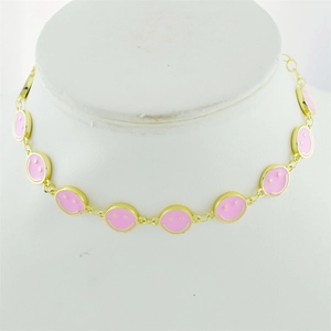 Detail of pink enamel smiley face charms on a gold-plated chain necklace worn on a model