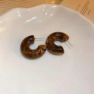 Close-up of amber tortoiseshell resin C-shaped hoop earrings on a white artistic plate