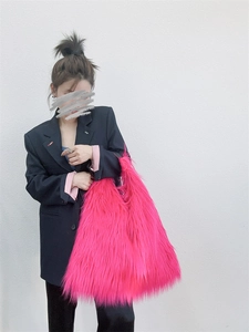 Detailed view of large hot pink faux fur tote bag carried by a model in dark attire