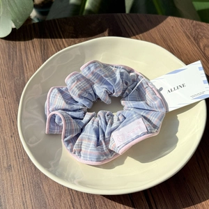 Close-up of a blue and pink plaid scrunchie with puppy label on a beige ceramic plate