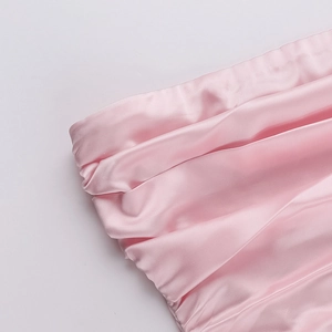 Close-up of pink satin fabric featuring pleated details and a glossy silk finish texture