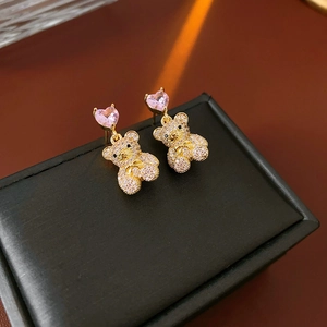 Détail de boucles d'oreilles ours dorées avec pierre de cœur rose et zircons blancs