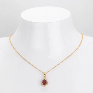 Macro shot of gold teardrop necklace with red gemstone and diamonds on a bust