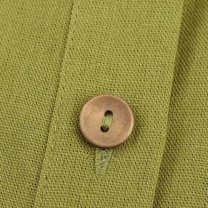 Macro shot of natural wooden button on green linen sleeveless dress fabric texture