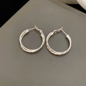 Close-up of silver-tone hoop earrings with intricate spiral woven texture design