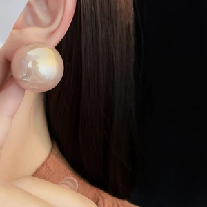 Close-up of a large champagne pink pearl stud earring worn on a model ear