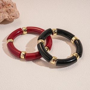 Dettaglio di bracciali in acrilico bordeaux e nero con inserti metallici dorati lucidi