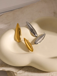 Macro shot of 18K gold and silver waterdrop earrings on a minimalist textured tray
