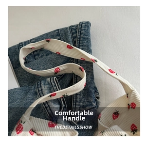 Detail of white corduroy tote bag showing strawberry print on wide flat handles