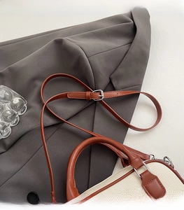 Close-up of adjustable brown leather shoulder strap and silver metal buckle on canvas bag