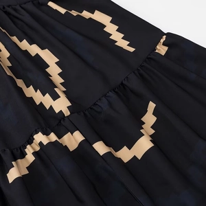 Dettaglio di abito boho con motivi geometrici dorati su tessuto nero plissettato