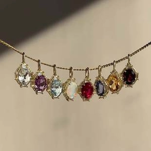 Dettaglio di otto ciondoli colorati con pietre portafortuna su catene d'oro sottili