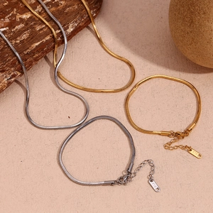 Close-up of 18K gold and silver snake chains with K18 engraved tags on wood and stone