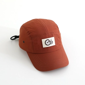 Detail view of brick red camper hat featuring white Go logo patch and breathable side eyelets