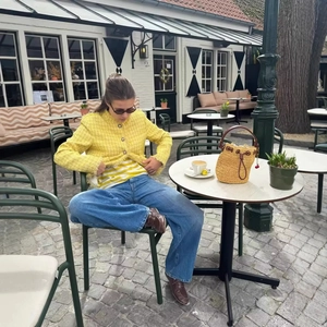 Outdoor shot of a bright yellow tweed jacket paired with a straw bag and blue jeans