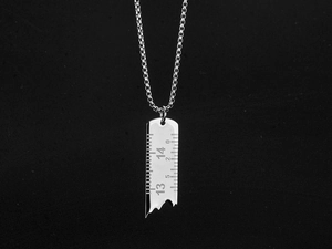 Vue détaillée du pendentif règle argenté avec graduations sur une chaîne boîte