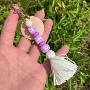 Détail de l'étiquette en bois, perles violettes HBD et pompon blanc sur porte-clés doré
