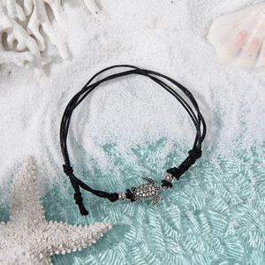 Detail shot of a silver turtle charm on a black braided cord anklet with beach shells