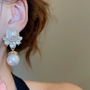 Close-up of elegant gold pearl drop earrings with rhinestones worn by a model