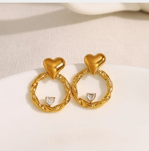 Close-up of golden heart earrings with twisted texture and crystal heart drop