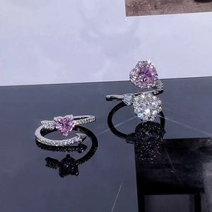 Close-up of pink heart-shaped crystal ring with white zircon stones on black mirror