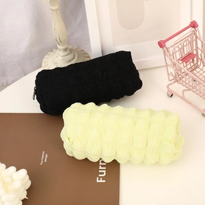 Detailed close-up of puff-textured pencil cases in black and soft yellow on desk