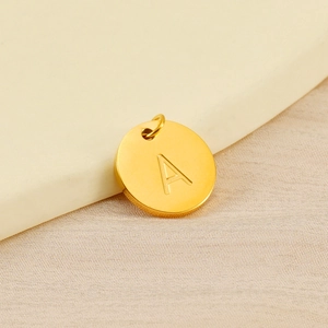 Macro shot of gold-plated circular pendant with a polished engraved capital letter A
