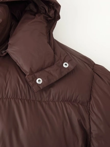 Détail d'une doudoune marron à capuche montrant le tissu brillant et les boutons pression