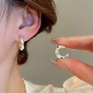 Detailed close-up of C-shaped enamel earrings with red and blue dots and golden stripes