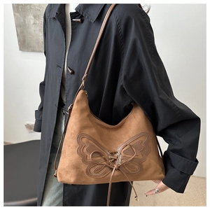 Gros plan sur un sac bandoulière en daim marron avec grand papillon et détails lacés